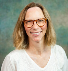Headshot of a smiling woman in glasses and a white shirt.
