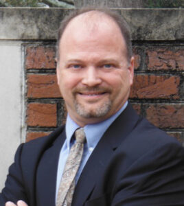 Headshot of a smiling man in a blue suit coat and light tie.