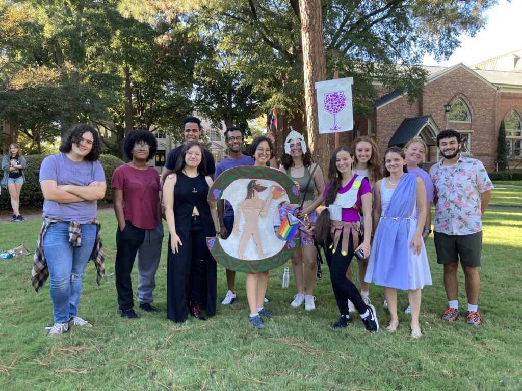 Students pose with their banner and shield on grass.