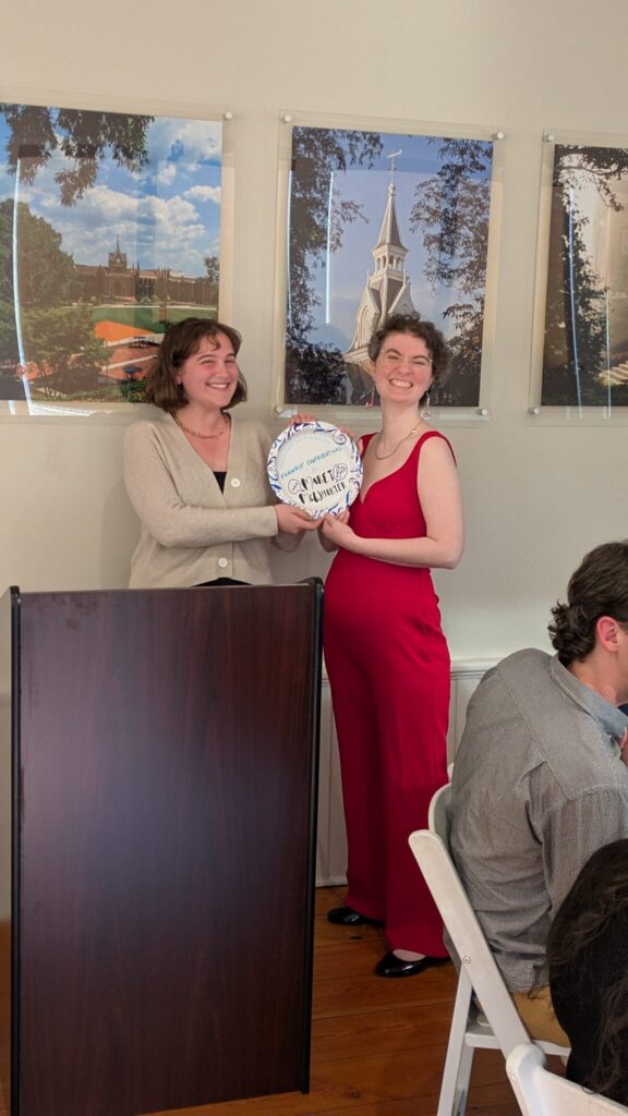 Two students stand next to a podium with a paper plate award.
