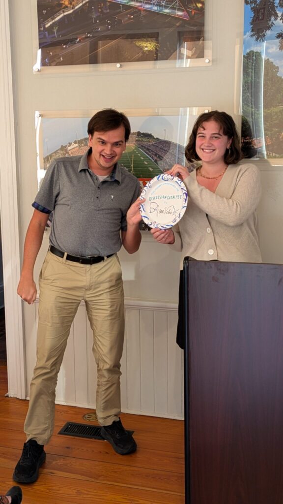 Two students stand next to a podium with a paper plate award.