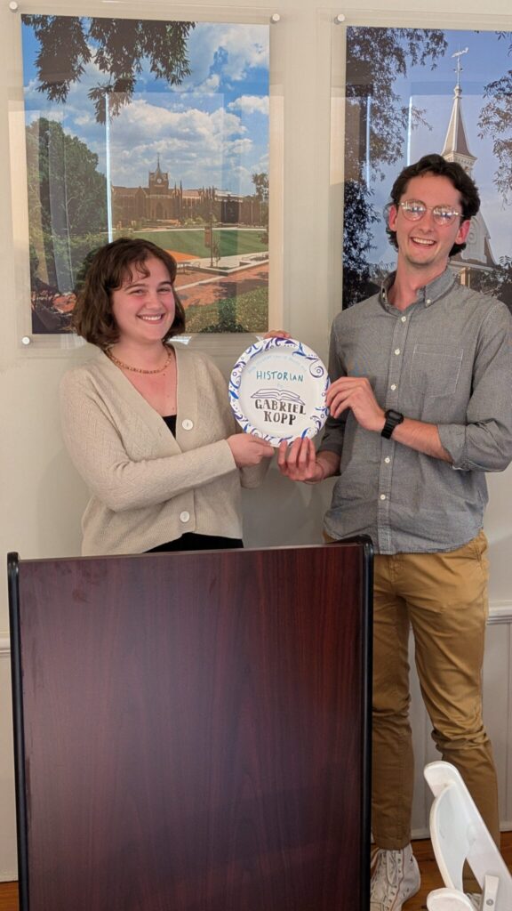 Two students stand behind the podium with a paper plate award.